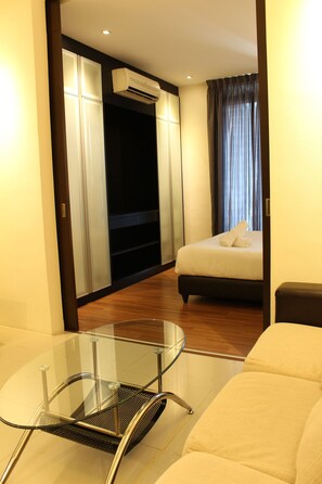 A hotel room with a bed, a glass table, a chair, a wardrobe, and an air conditioning unit.