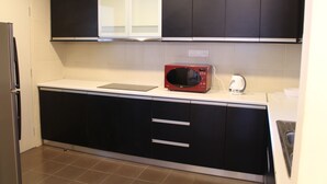 A kitchen with black cabinets, a white countertop, a red microwave, and a kettle. - Peaceful Service Suites at Taragon Puteri Bintang (Kuala Lumpur)
