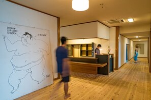 A hotel lobby with a reception desk, wooden flooring, and a large whiteboard with a cartoon drawing. - ZABaN shikanoshima (Fukuoka)