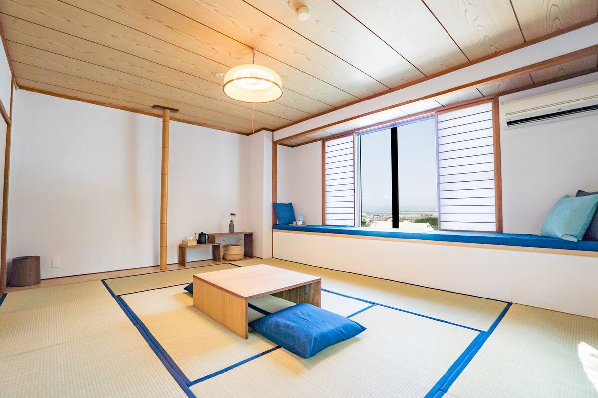 Habitació japonesa tradicional amb sòls de tatami, una taula de fusta baixa, una finestra amb vista i un ventilador de sostre.