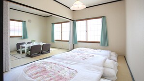Una habitación de hotel con dos camas, un área de comedor con mesa y sillas, y ventanas amplias con cortinas.
