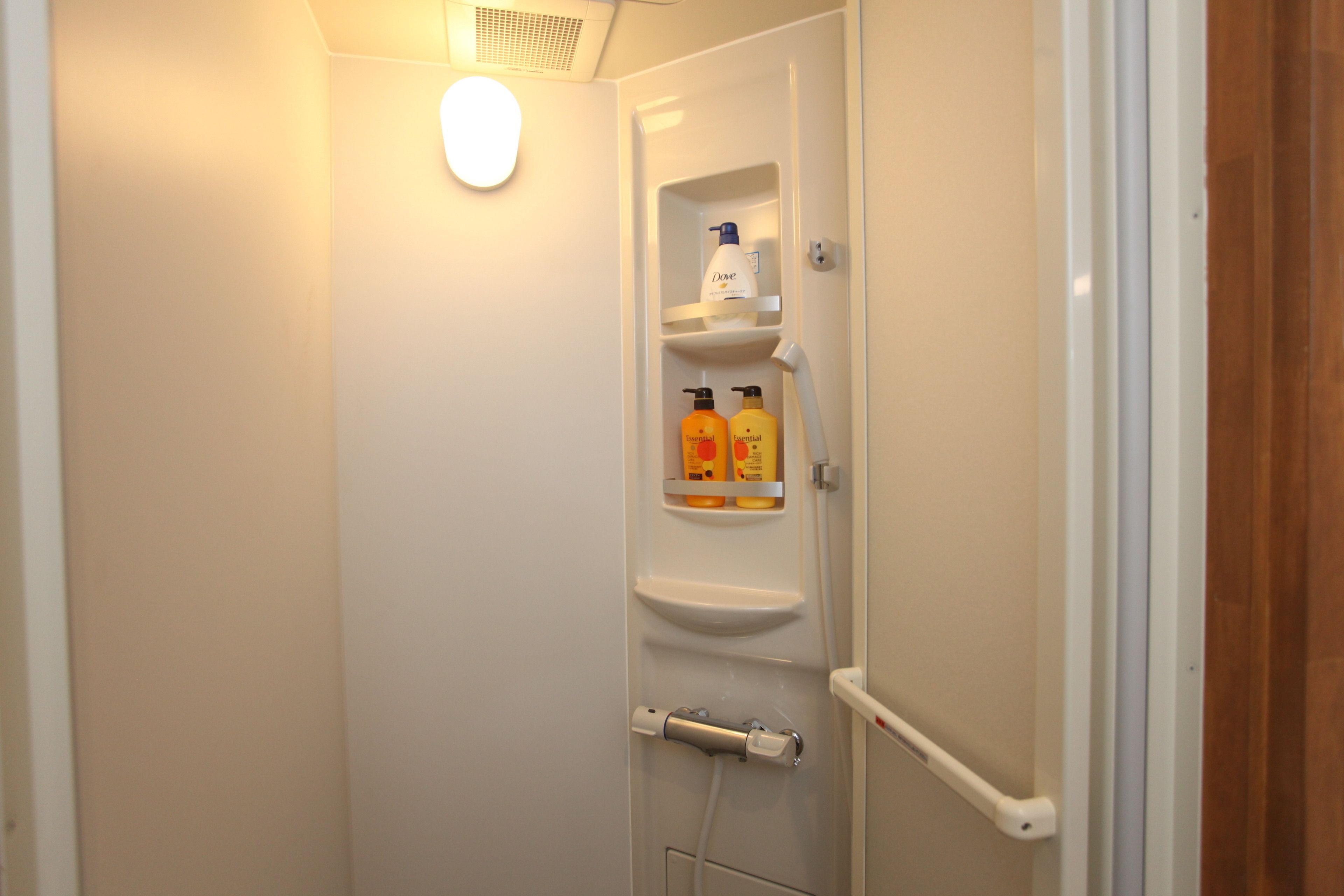 A bathroom with a shower, a toilet, and a shelf with toiletries.