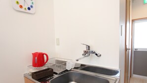 Una cocina con un lavamanos doble, una tetera roja, un escurreplatos y un reloj de pared.