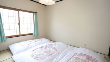 A room with tatami flooring, a bed with floral bedding, a window with curtains, and a ceiling light fixture.