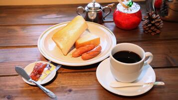 Uma mesa de madeira com uma fatia de pão torrado e salsichas, uma chávena de café, um bule e uma pequena tigela com compota e uma faca.