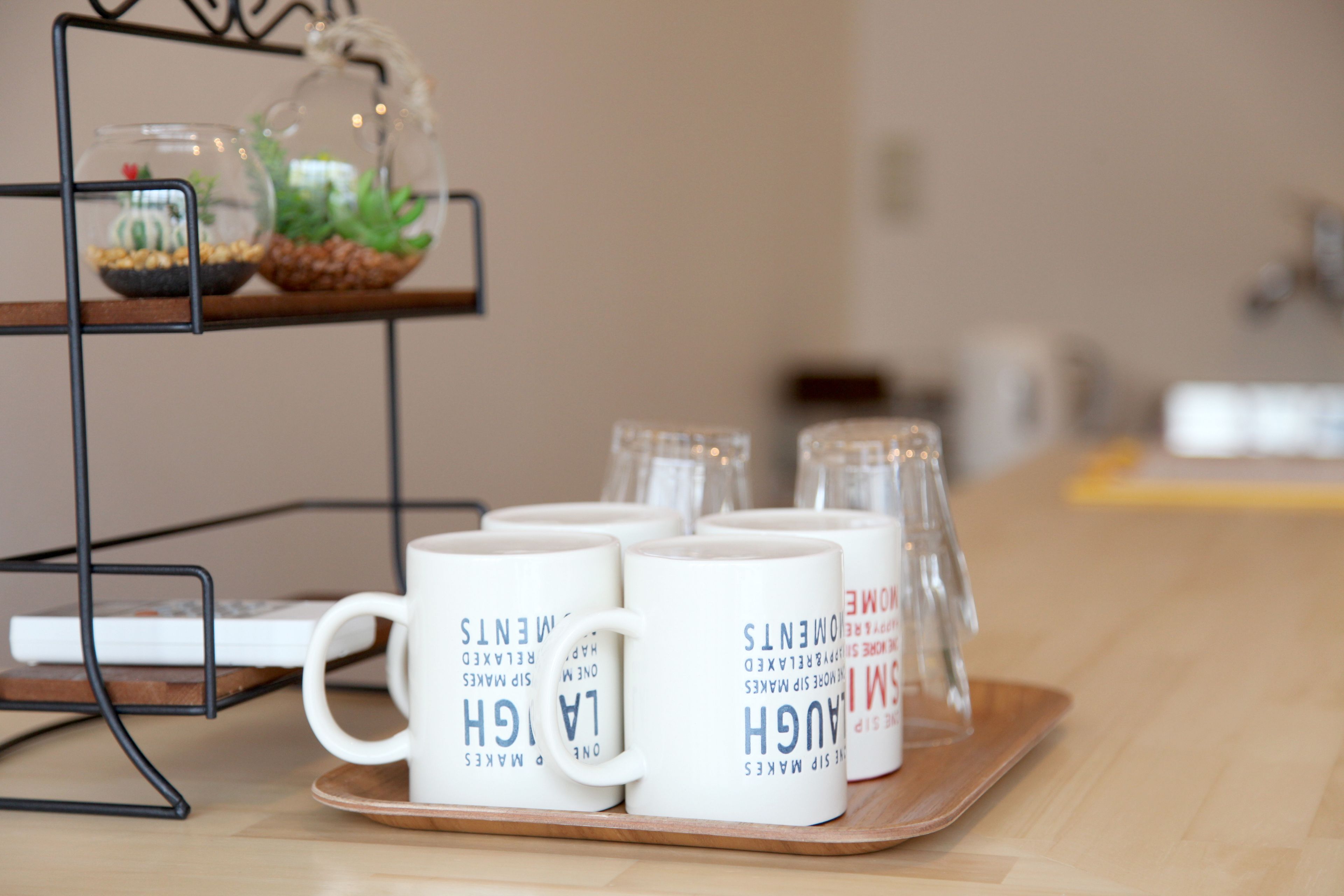 A tray with white mugs and a small glass terrarium on a wooden table.