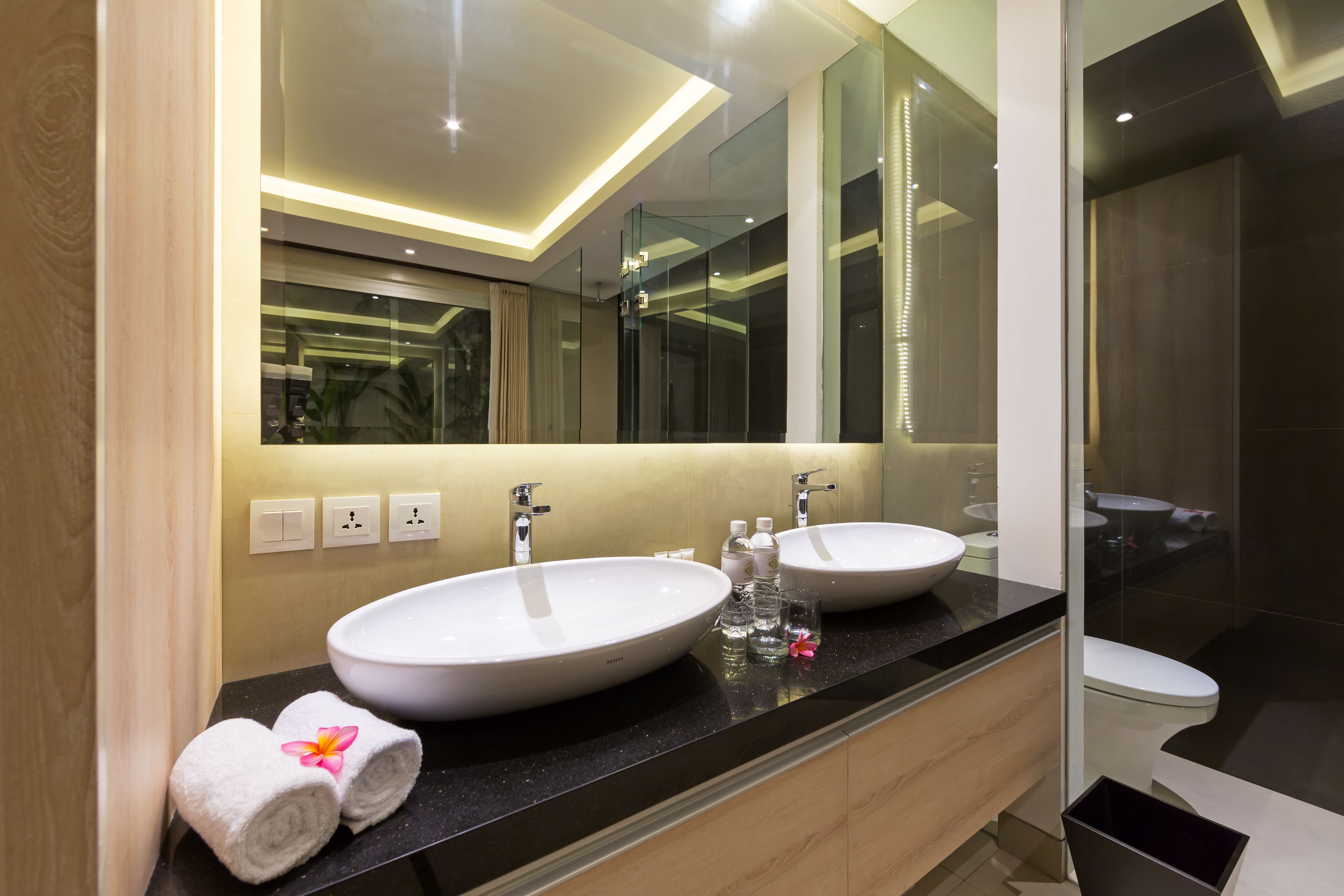 Une salle de bain moderne avec deux grands lavabos blancs, un plan de toilette noir et un grand miroir.