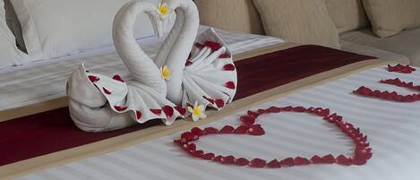 A bed with a swan-shaped towel arrangement and heart-shaped flower petals on the bedspread.