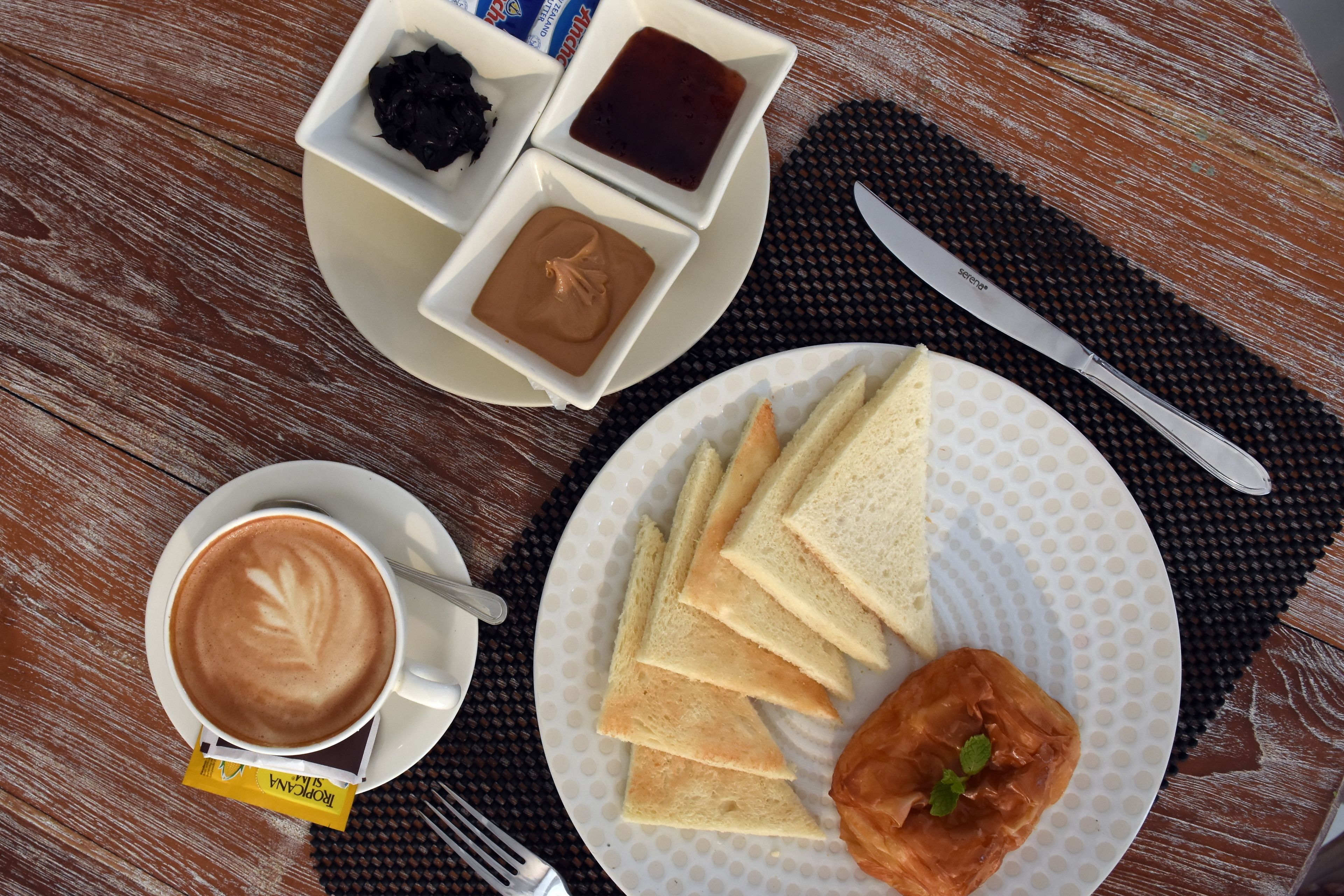 A breakfast setting with a cup of coffee, a plate of toast, and small bowls containing condiments.