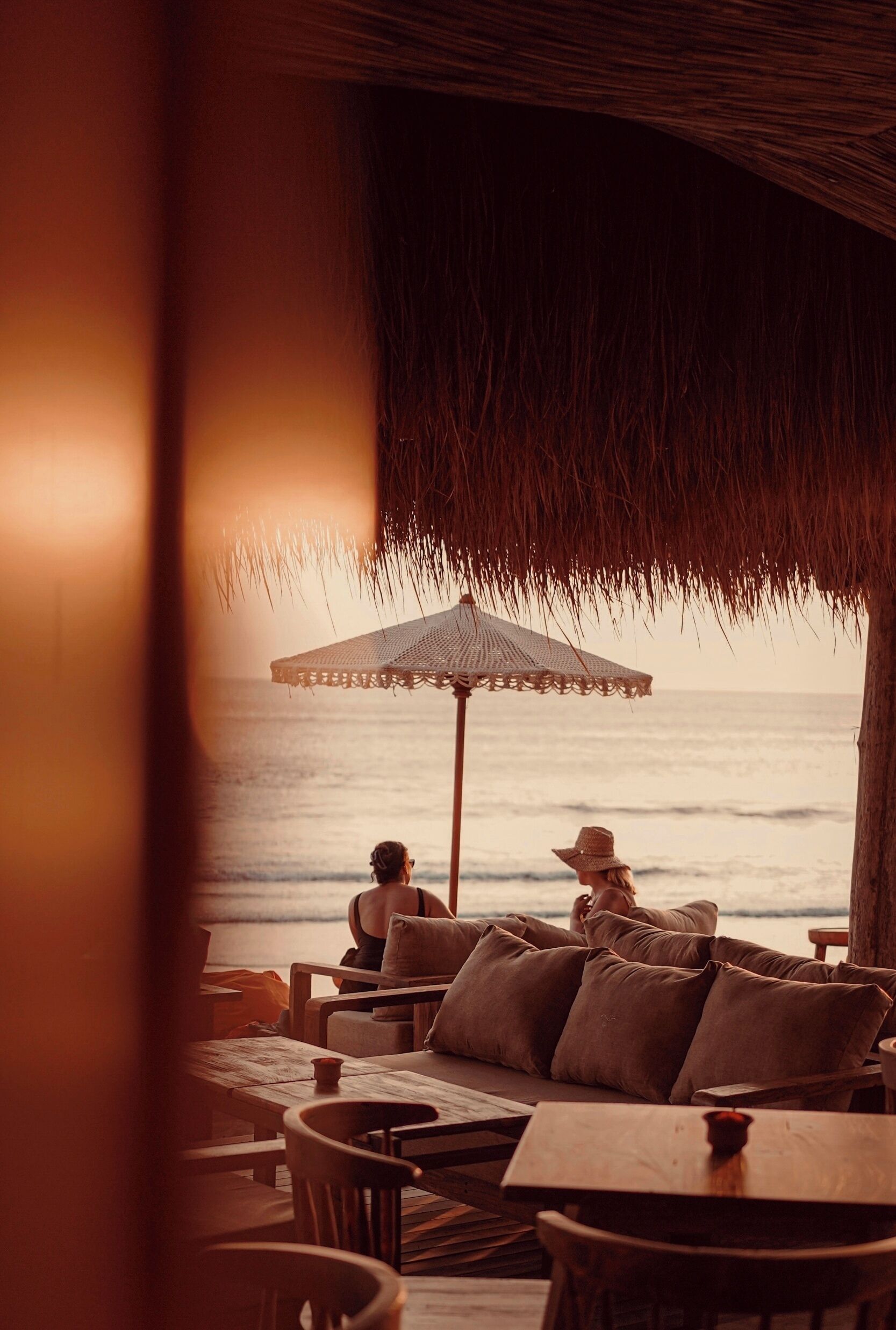 A beachside lounge with a thatched roof, wooden furniture, and a view of the ocean.
