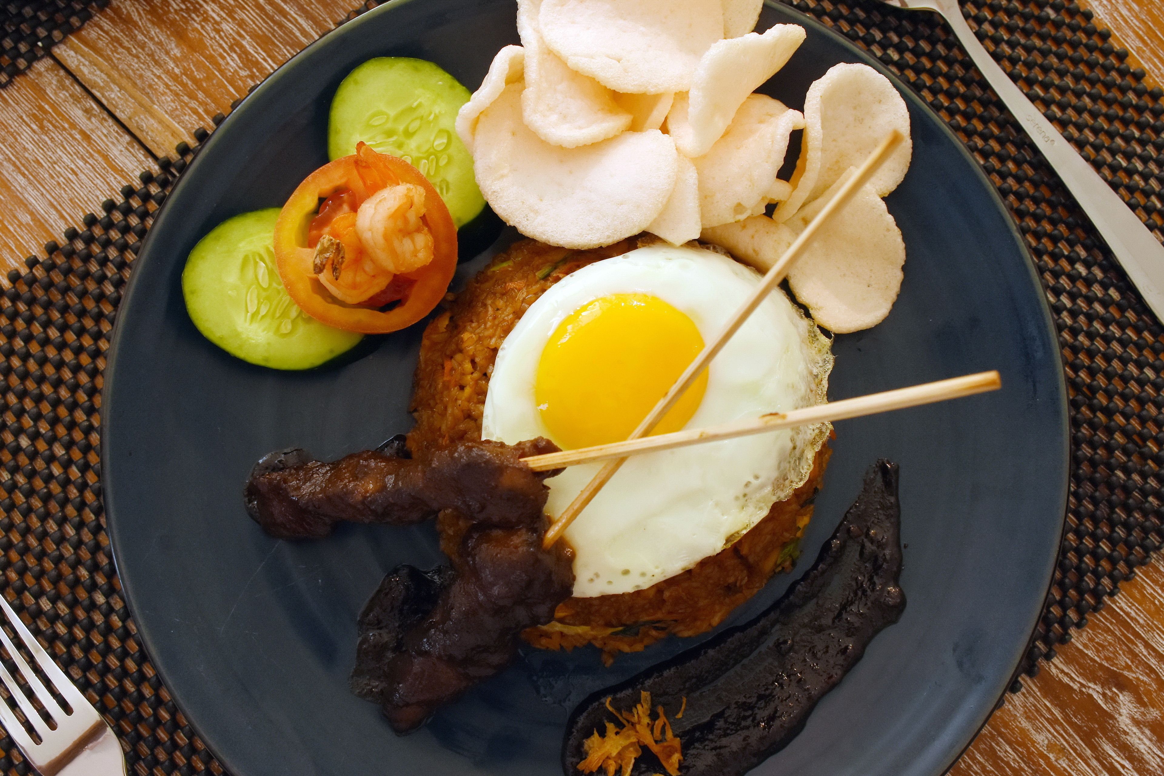 A plate with a fried egg, skewered meat, slices of cucumber, tomato, and chips.