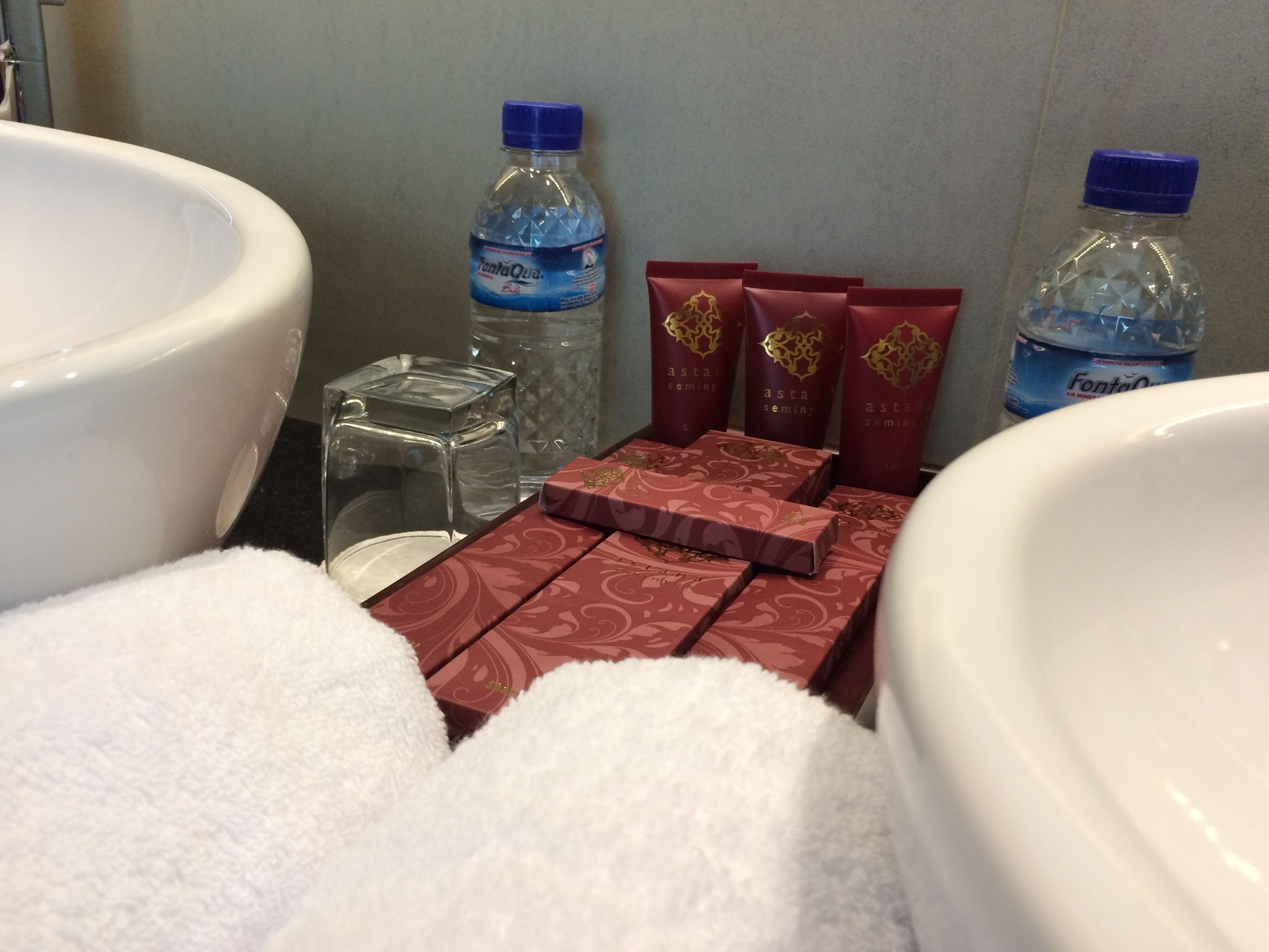 Un baño con una bañera blanca grande, un recipiente de vidrio y varias cajas rojas de artículos de aseo.