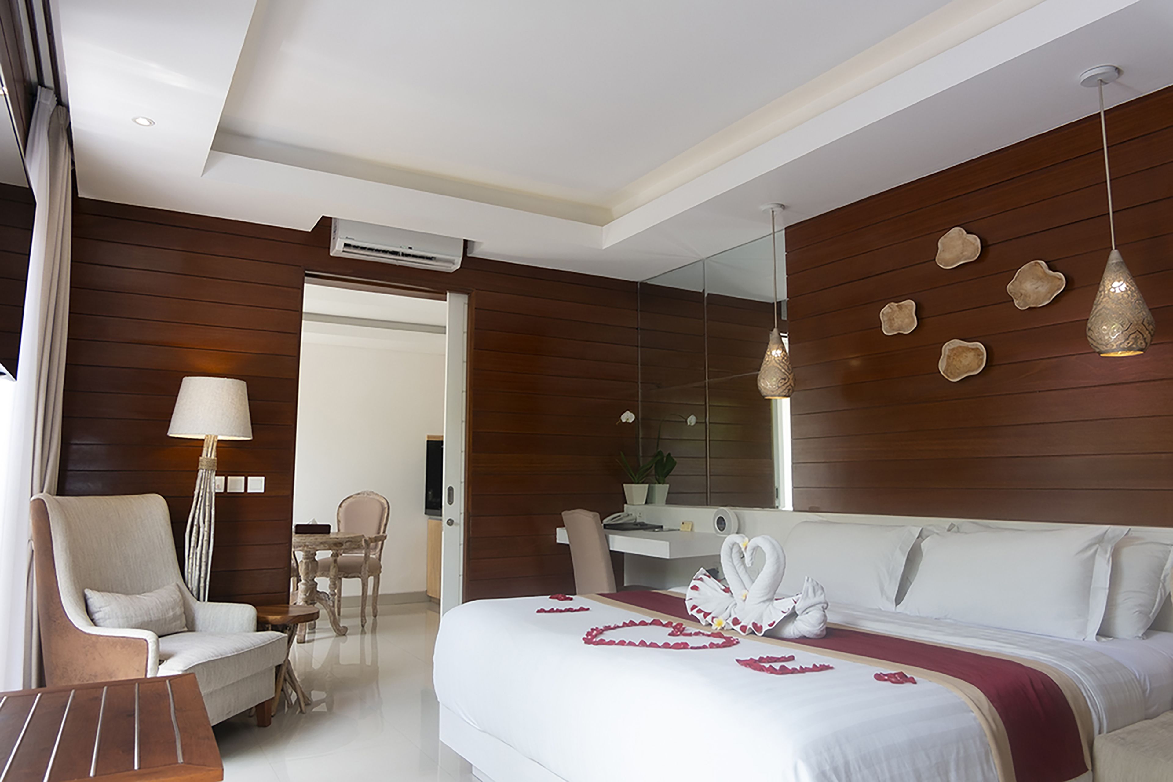 Une chambre d’hôtel moderne dotée d’un grand lit, d’un coin salon avec un fauteuil et une table, d’un bureau et d’un miroir au mur.