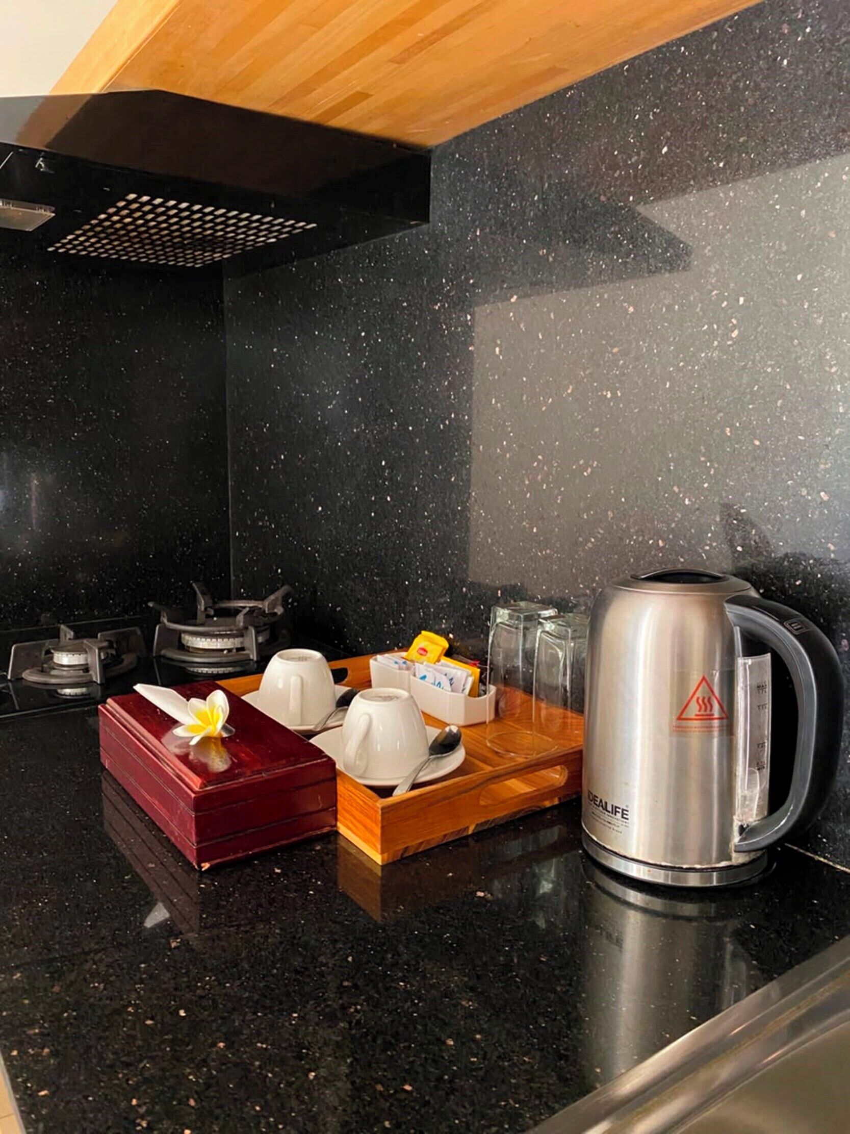 A kitchen with a black countertop, a coffee maker, and a tray with cups and a flower.