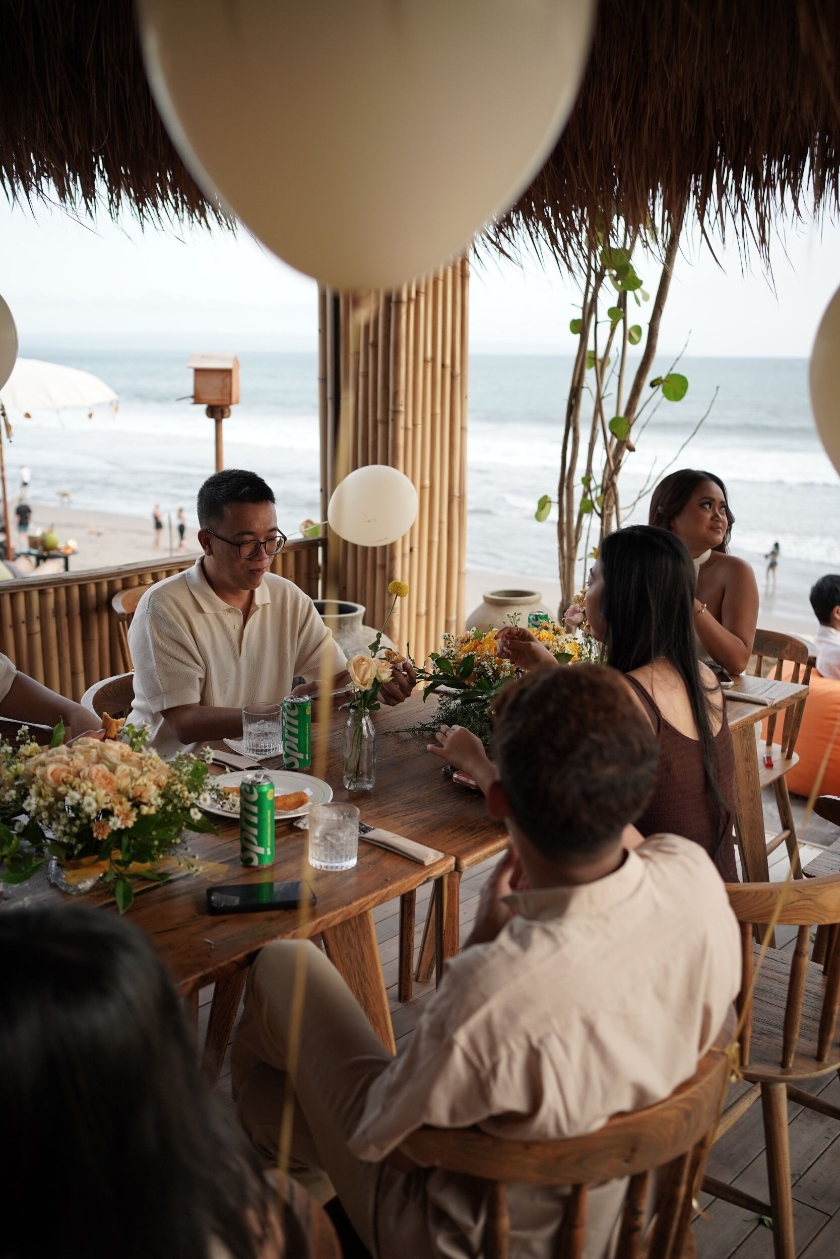 Una mesa de madera con sillas, techo de paja y vista a la playa.