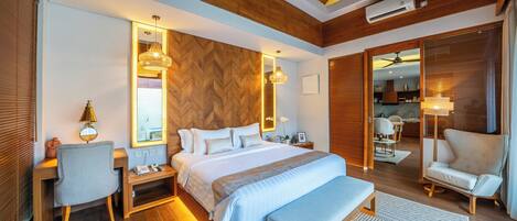 A modern hotel room with a wooden ceiling, a large bed with a blue bedspread, a desk with a lamp, and a seating area with a chair and bench.