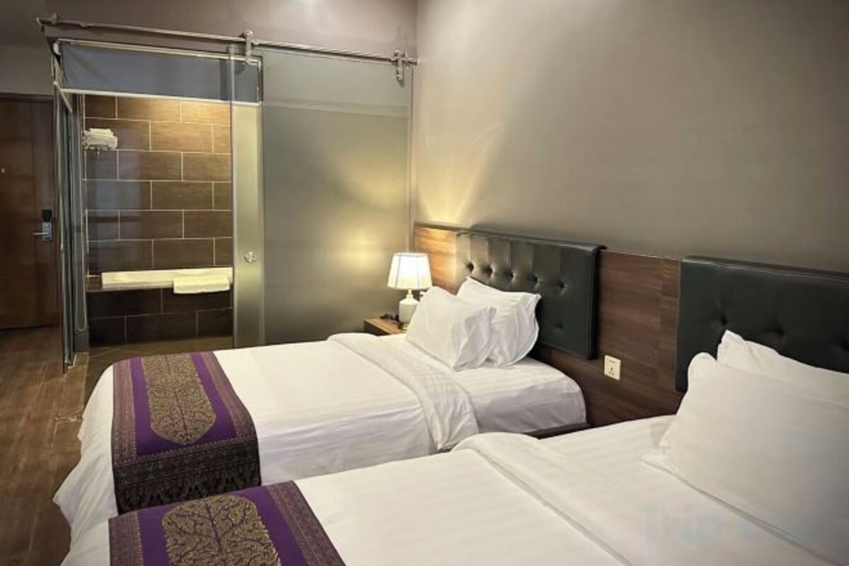 Una habitación de hotel con dos camas, una ducha y una mesita de noche con lámpara.