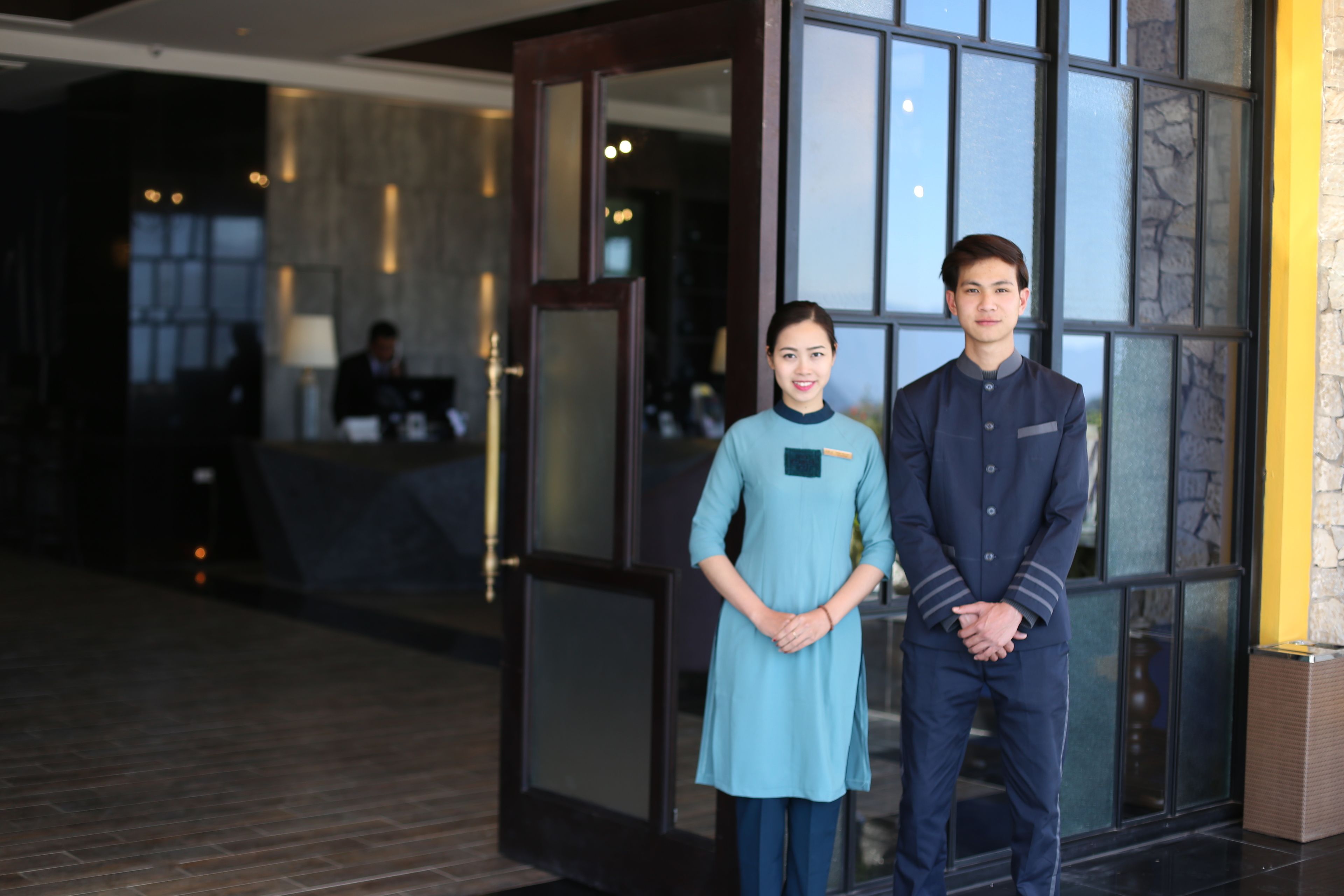 A hotel lobby with a reception desk, a large window with a view, and a person in a uniform standing in front of the window.