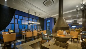 Un área lounge moderna con una chimenea central, asientos y vistas a la ciudad a través de amplios ventanales.