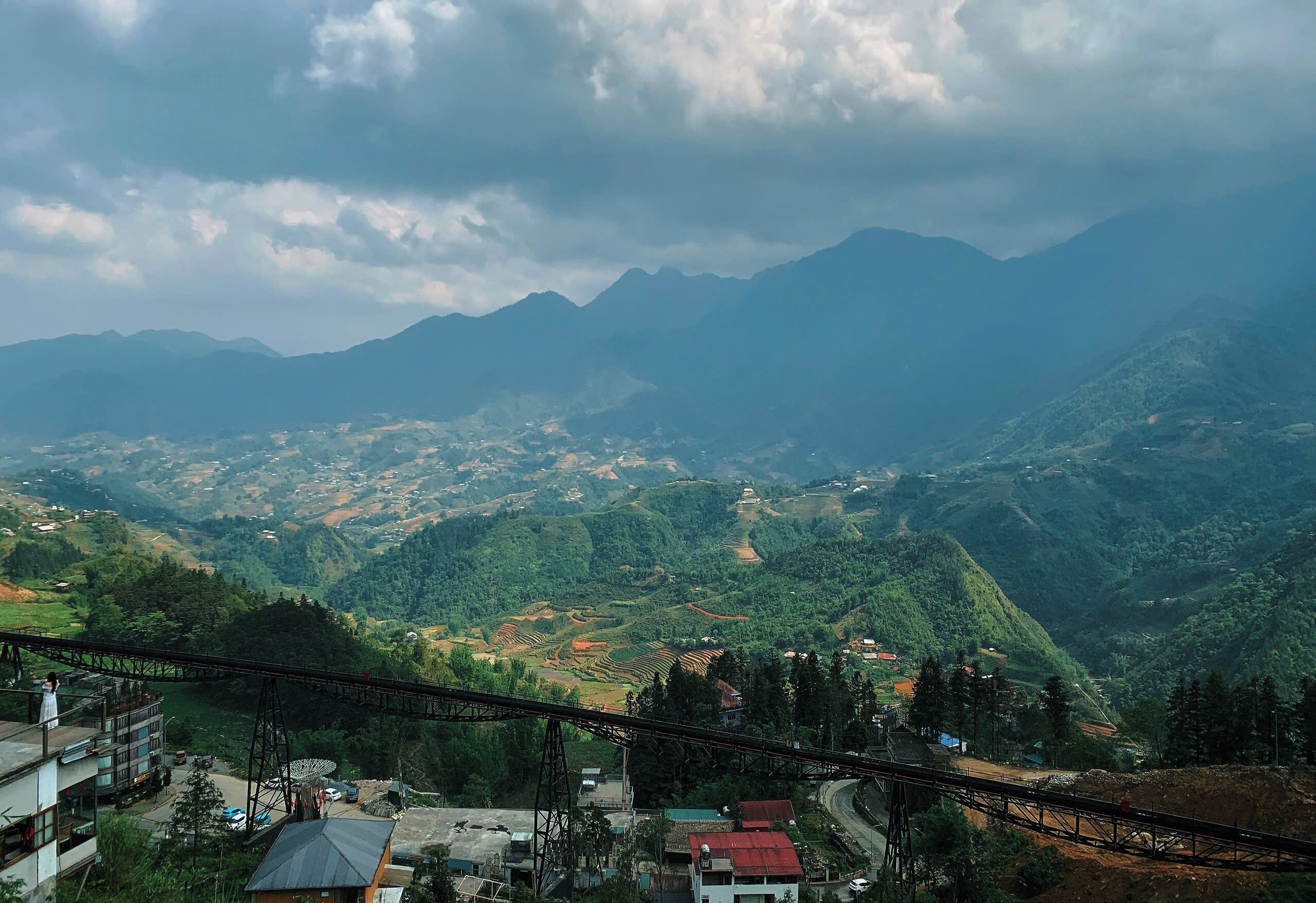 A mountainous landscape with terraced fields, a bridge, and scattered buildings.