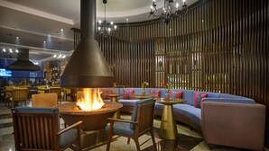 Un área de estar moderna con una chimenea central, disposición de asientos y un muro decorativo.
