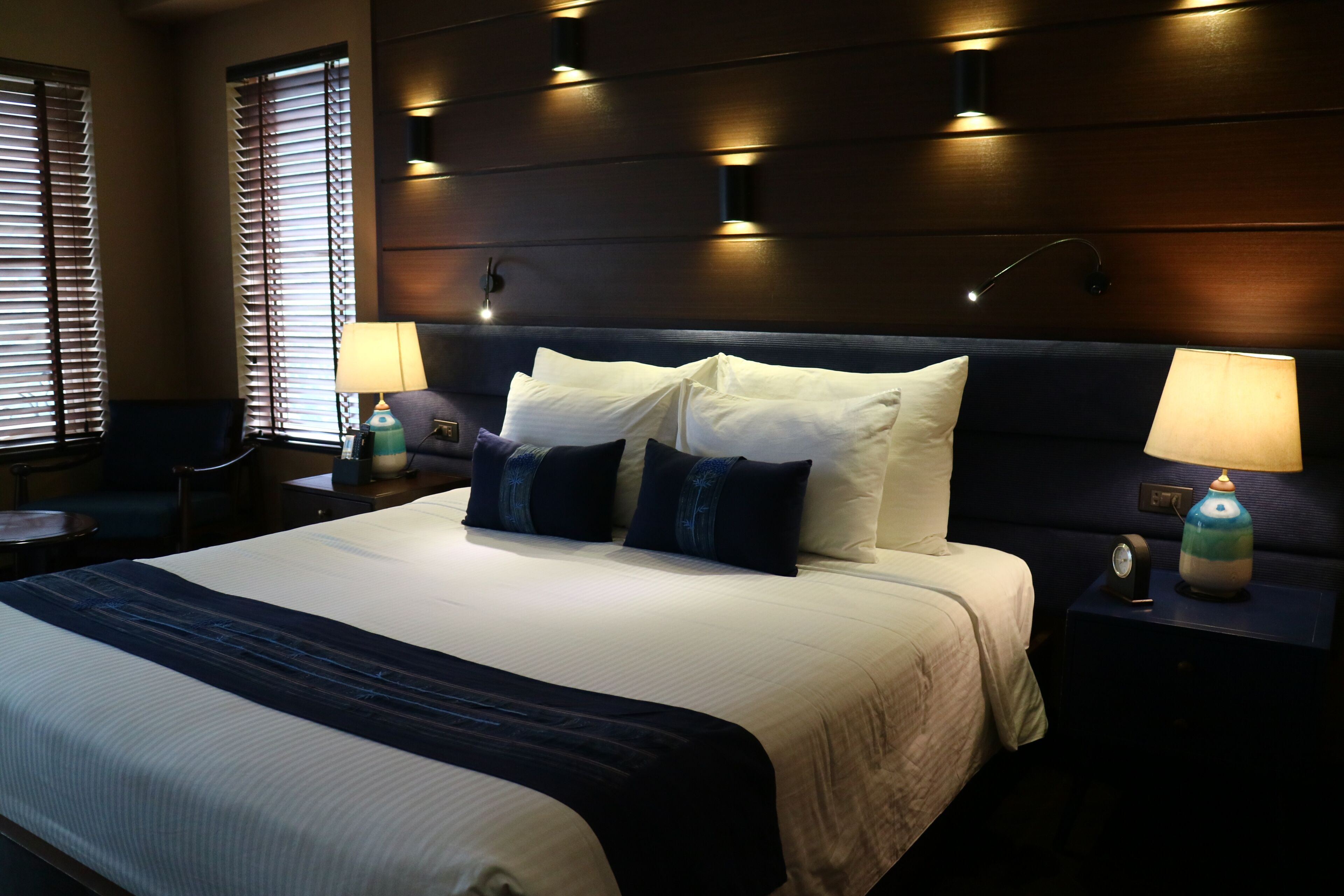 A hotel room with a large bed, two bedside tables, a nightstand, and a wall-mounted lamp.