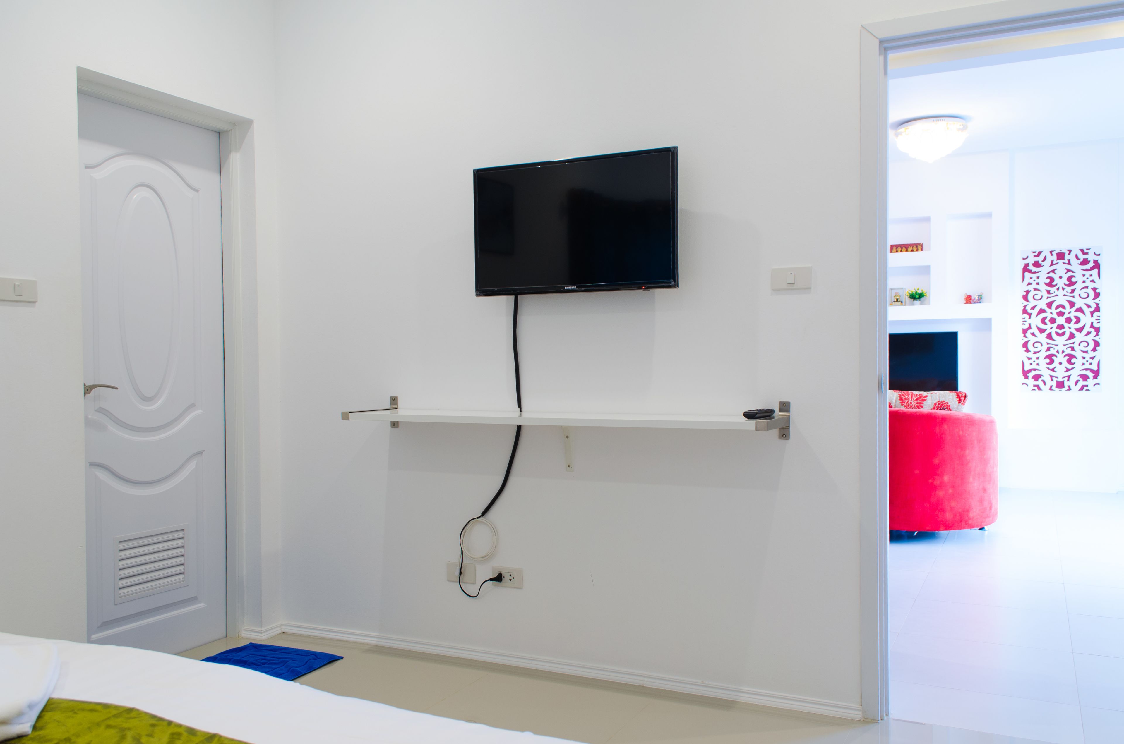 A room with a mounted flat-screen TV, a white door, and a red ottoman in the background.