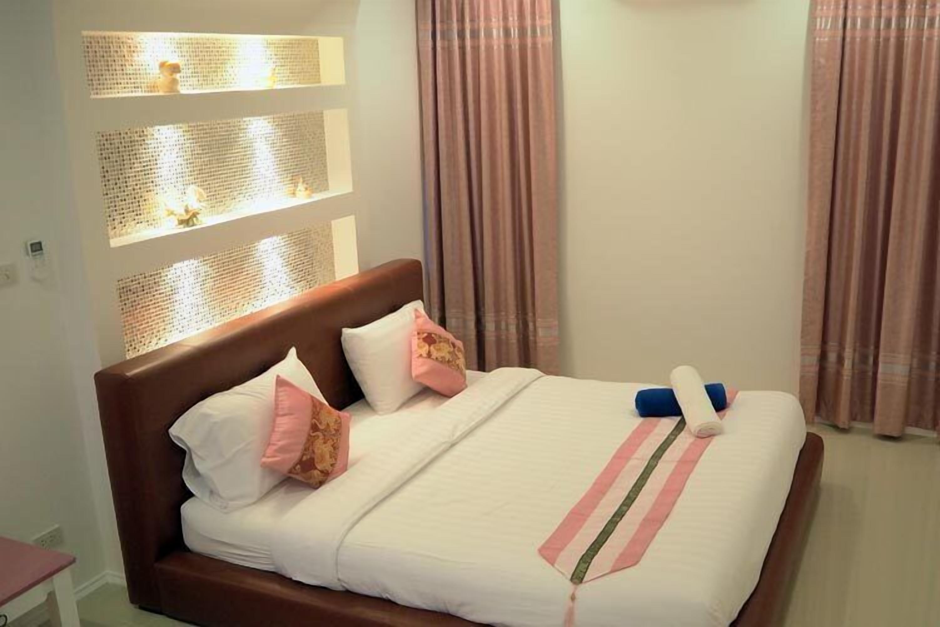 A neatly made bed with a white and pink striped bedspread, a brown headboard, and a small nightstand with a lamp.