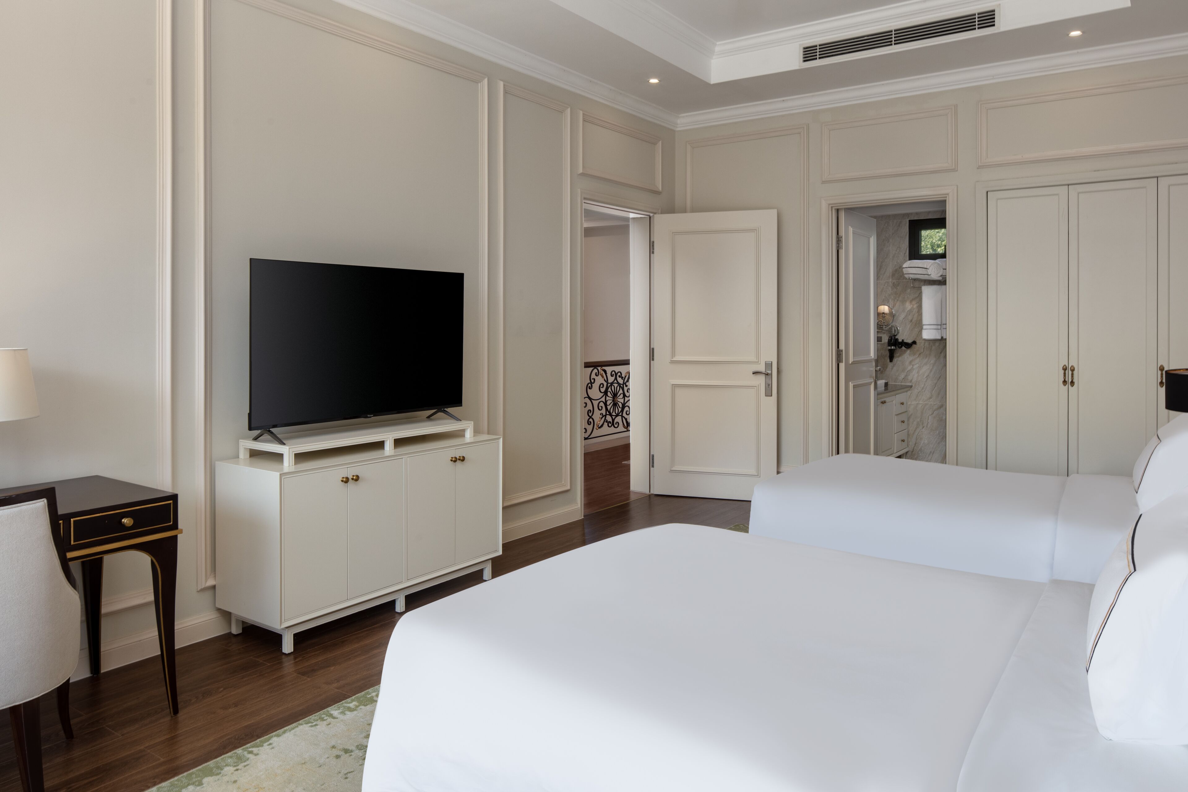 A hotel room with a large bed, a TV on a cabinet, a desk with a lamp, and a wardrobe.