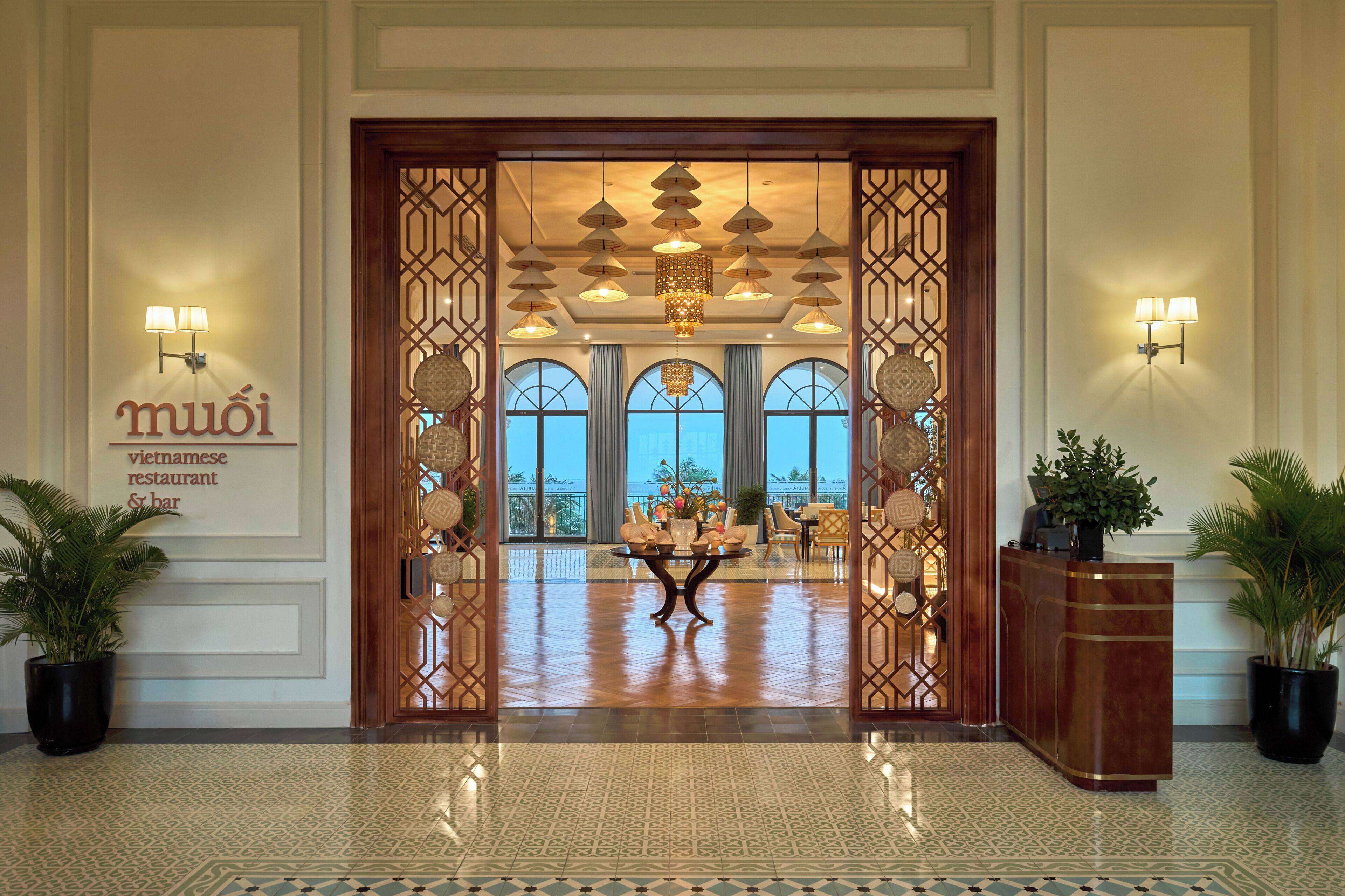 A hotel lobby with a reception desk, a decorative entrance, and a view of the outdoors.