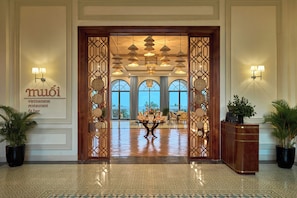A hotel lobby with a reception desk, a decorative entrance, and a view of the outdoors. - Melia Vinpearl Cam Ranh Beach Resort (Cam Lam)