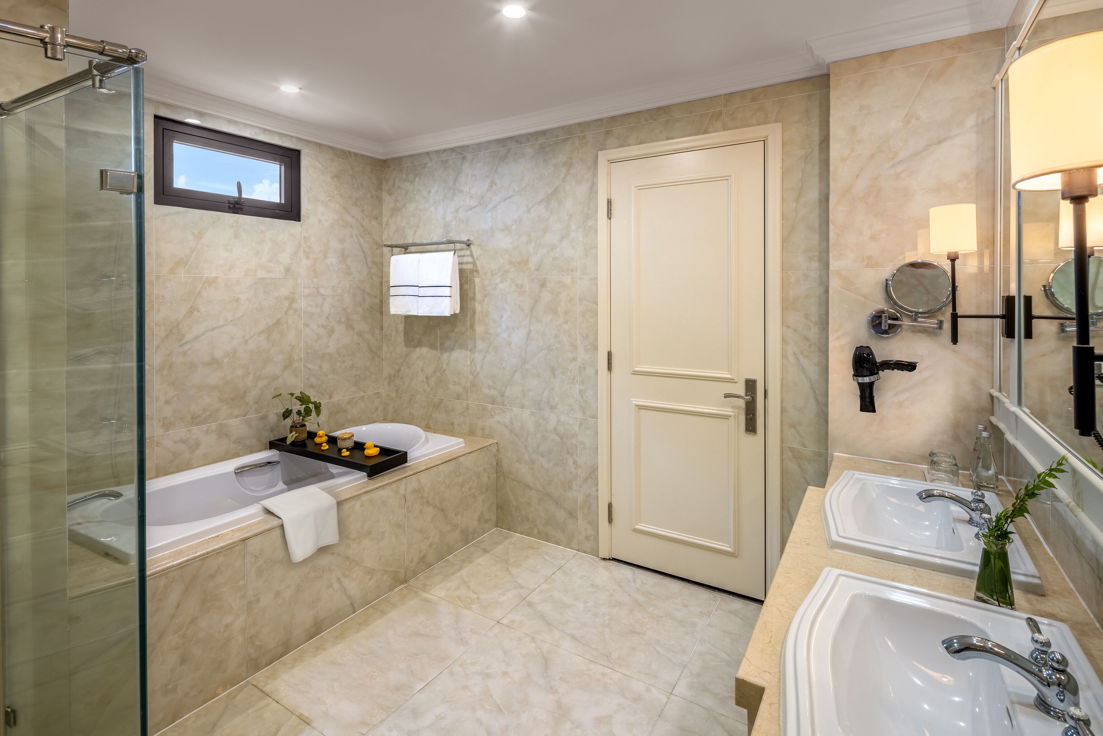 A modern bathroom with a glass shower enclosure, a freestanding bathtub, two sinks, and a large mirror.
