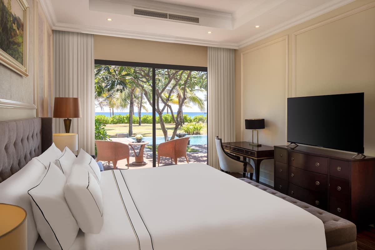 A hotel room with a large bed, a desk, a television, and a view of palm trees and a pool.