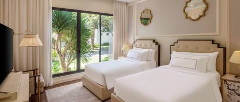 A hotel room with two beds, a TV, a desk, and a large window with a view of palm trees.
