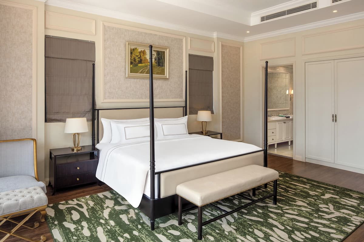 A four-poster bed with a bench, a nightstand with a lamp, a mirror, and a wardrobe in a hotel room.