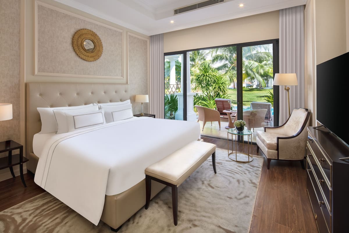 A hotel room with a large bed, a bench, a TV, a chair, and a view of the outdoors.