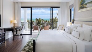 A hotel room with a large bed, a desk, and a balcony with a view of the ocean.