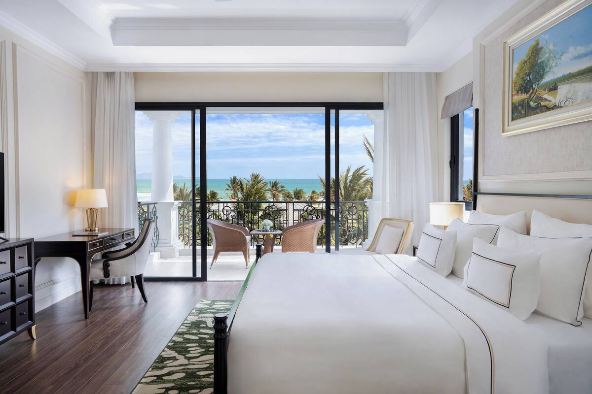 A hotel room with a large bed, a desk, and a balcony with a view of the ocean.
