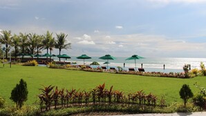 A poolside area with green umbrellas, palm trees, and a view of the sea. - Ocean Front Campgrounds (Ngwe Saung)