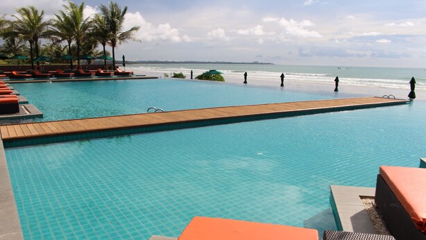 A pool with a wooden deck, lounge chairs, and palm trees. - Ocean Front Campgrounds (Ngwe Saung)