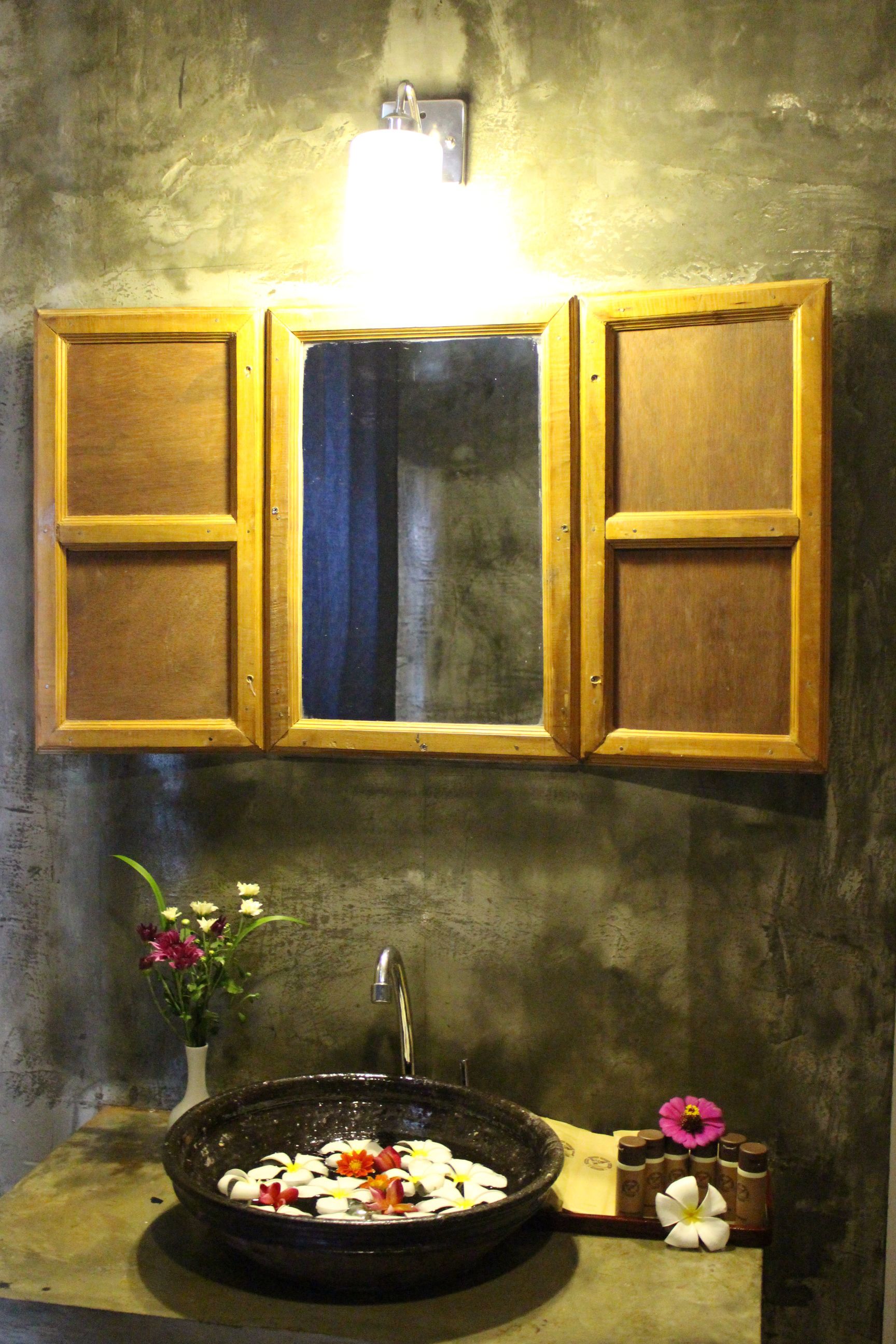 A bathroom with a wooden cabinet above a sink, a mirror, and a light fixture.