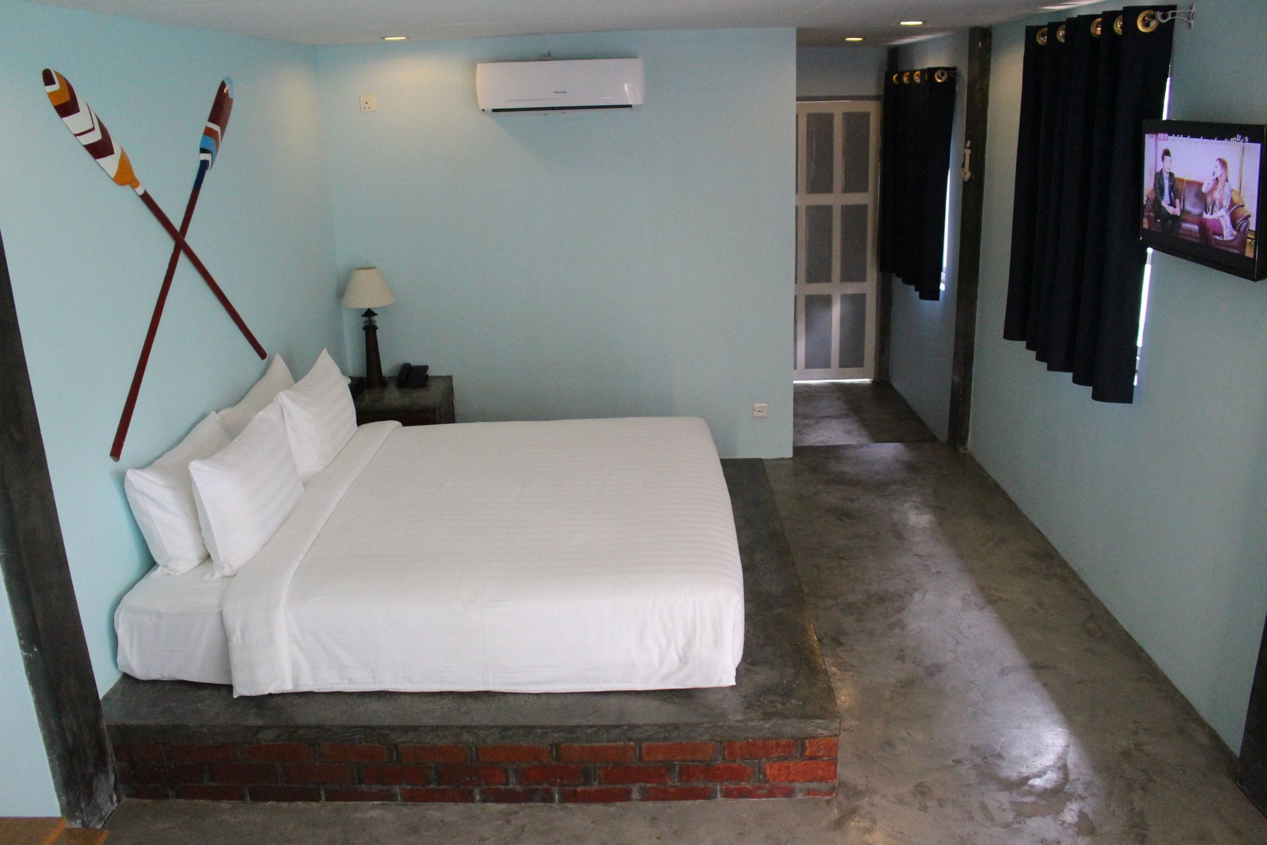Un dormitorio con una cama, una mesita de noche, una lámpara, un televisor y un aire acondicionado instalado en la pared.