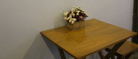 A framed nautical-themed artwork on a wall, a wooden table with a basket of flowers, and a small wooden stool.