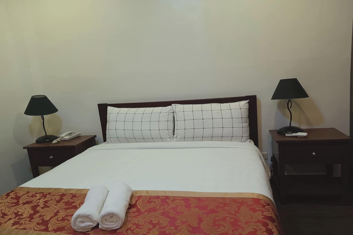 A neatly made bed with a patterned bedspread, two bedside lamps, a nightstand with a phone, and a remote control.
