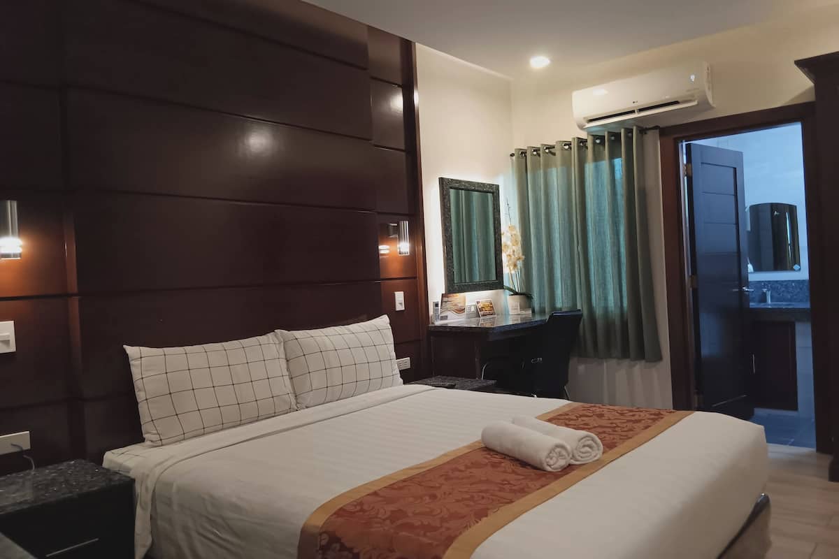 A hotel room with a large bed, a desk with a chair, a mirror, and a view of the outside.