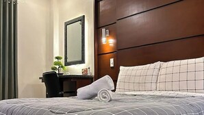Une chambre d’hôtel moderne avec un grand lit, une tête de lit en bois, un bureau avec une chaise et un miroir.
