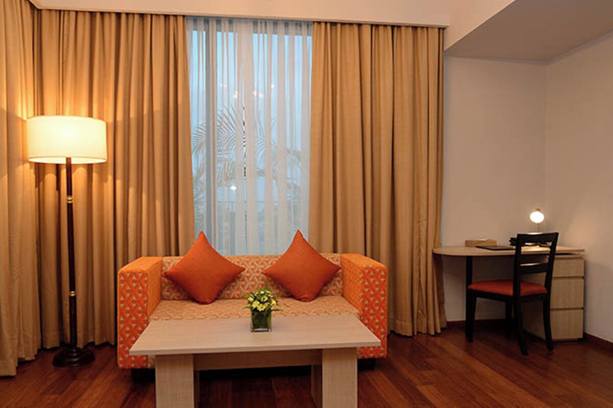 Una habitación de hotel con sofá, una mesa con un florero, un escritorio y una lámpara.