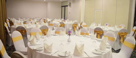 A banquet hall with round tables set for dining, white chairs with gold sashes, and a neutral color scheme.