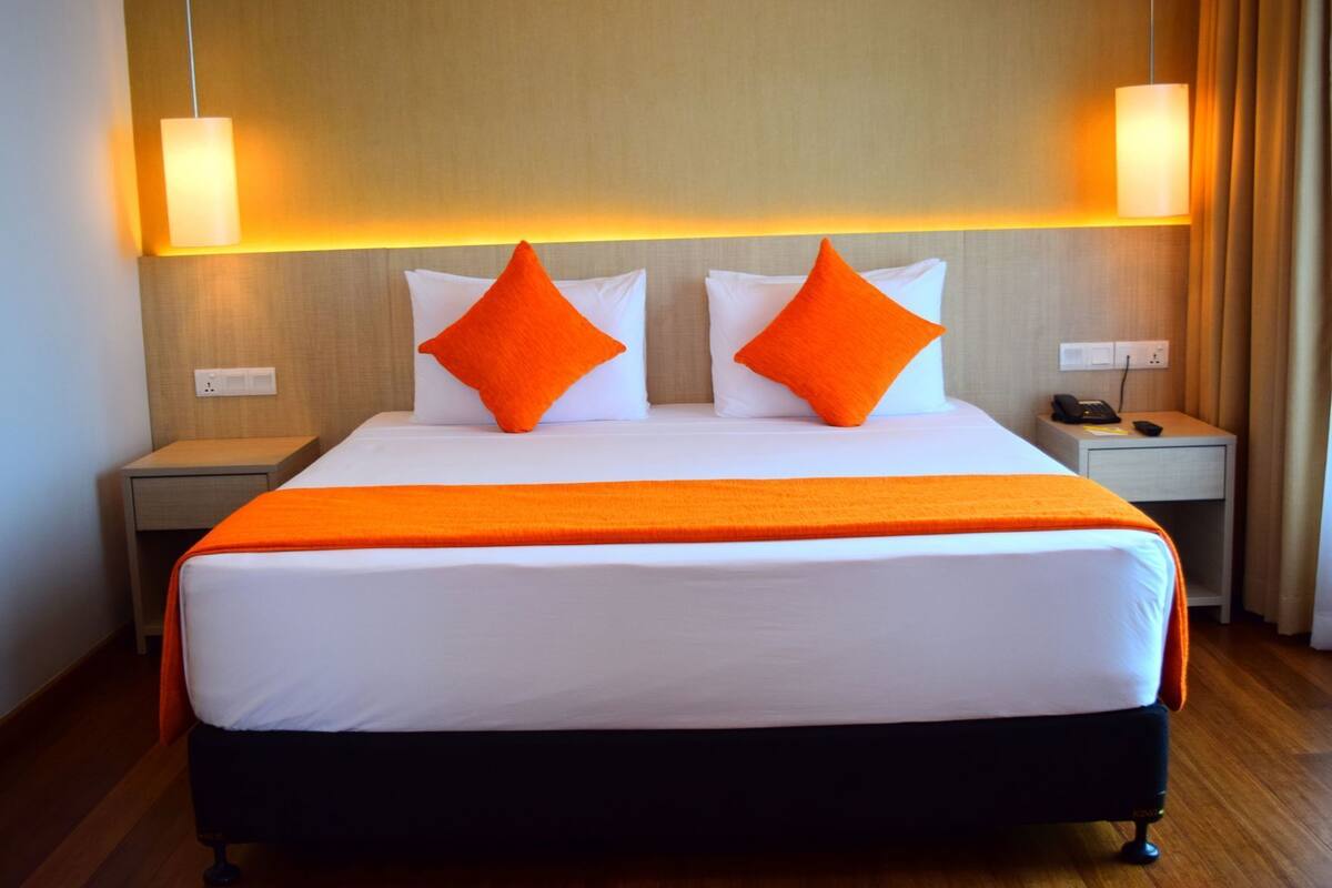 A hotel room with a large bed, two nightstands, a telephone, and a wall-mounted lamp.