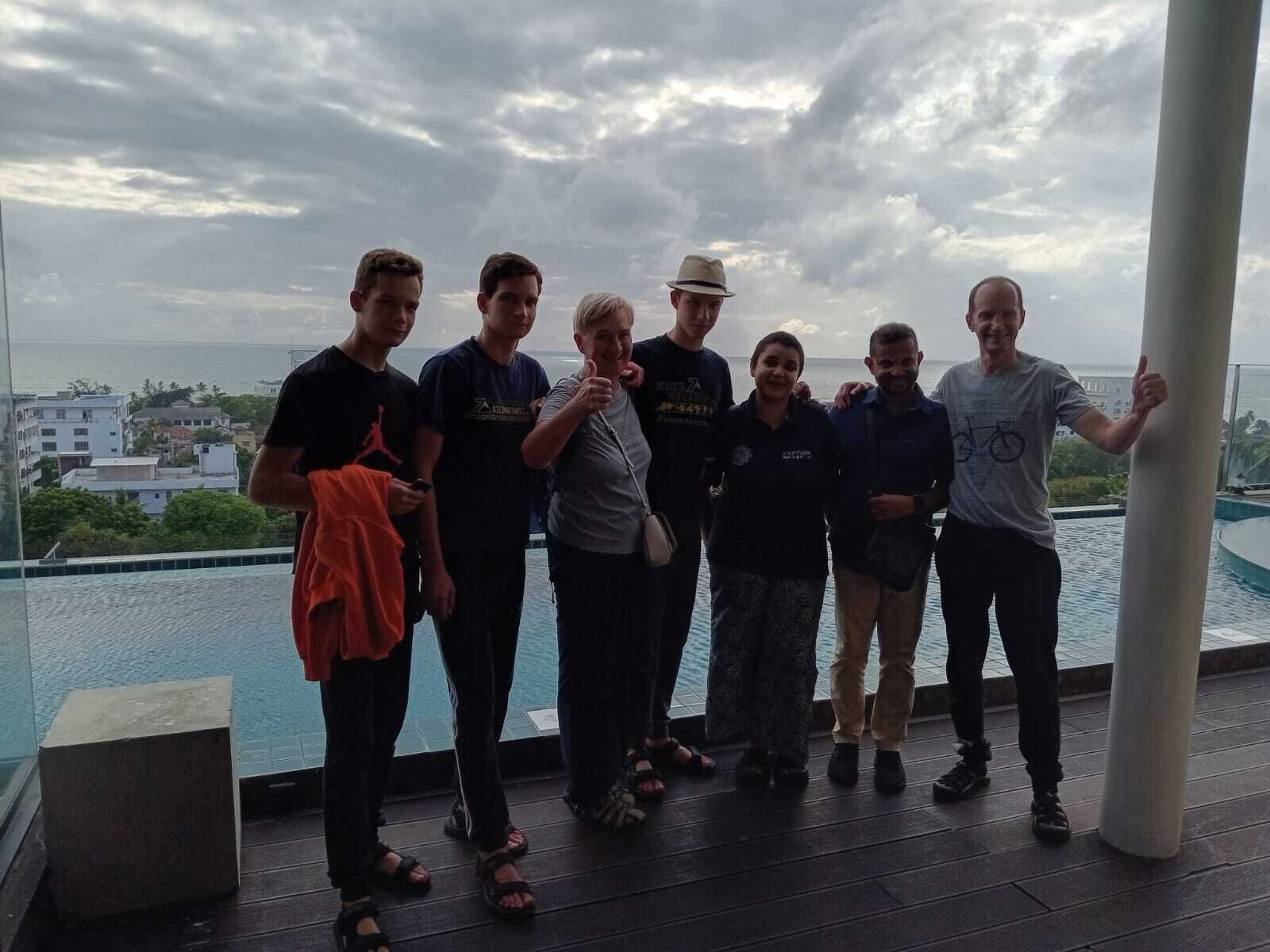 A group of people standing on a rooftop terrace with a view of the sea and buildings in the background.